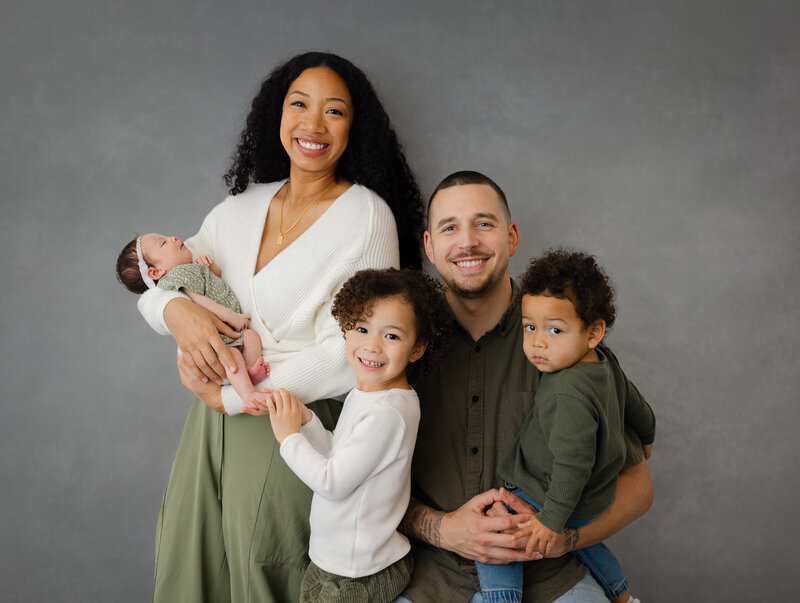 Newborn family session with mom holding baby in a green onesie and dad holding son wearing a similar shade of green. 