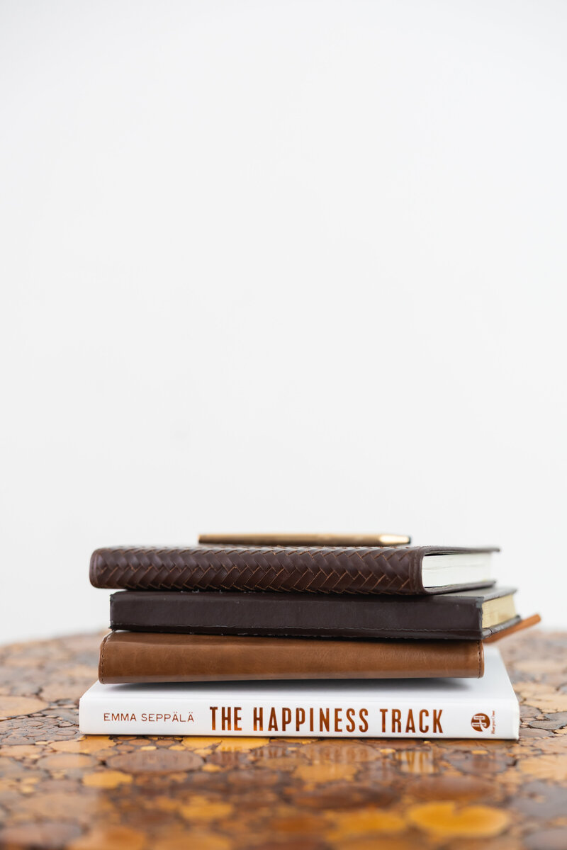 Stack of journals and The Happiness Track book symbolizing reflection and growth