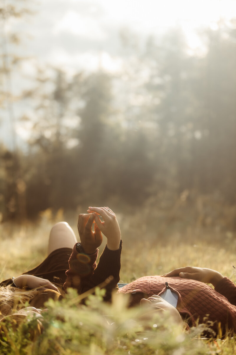 Couple lying in tall grass under a moody sky, embodying natural and raw connection