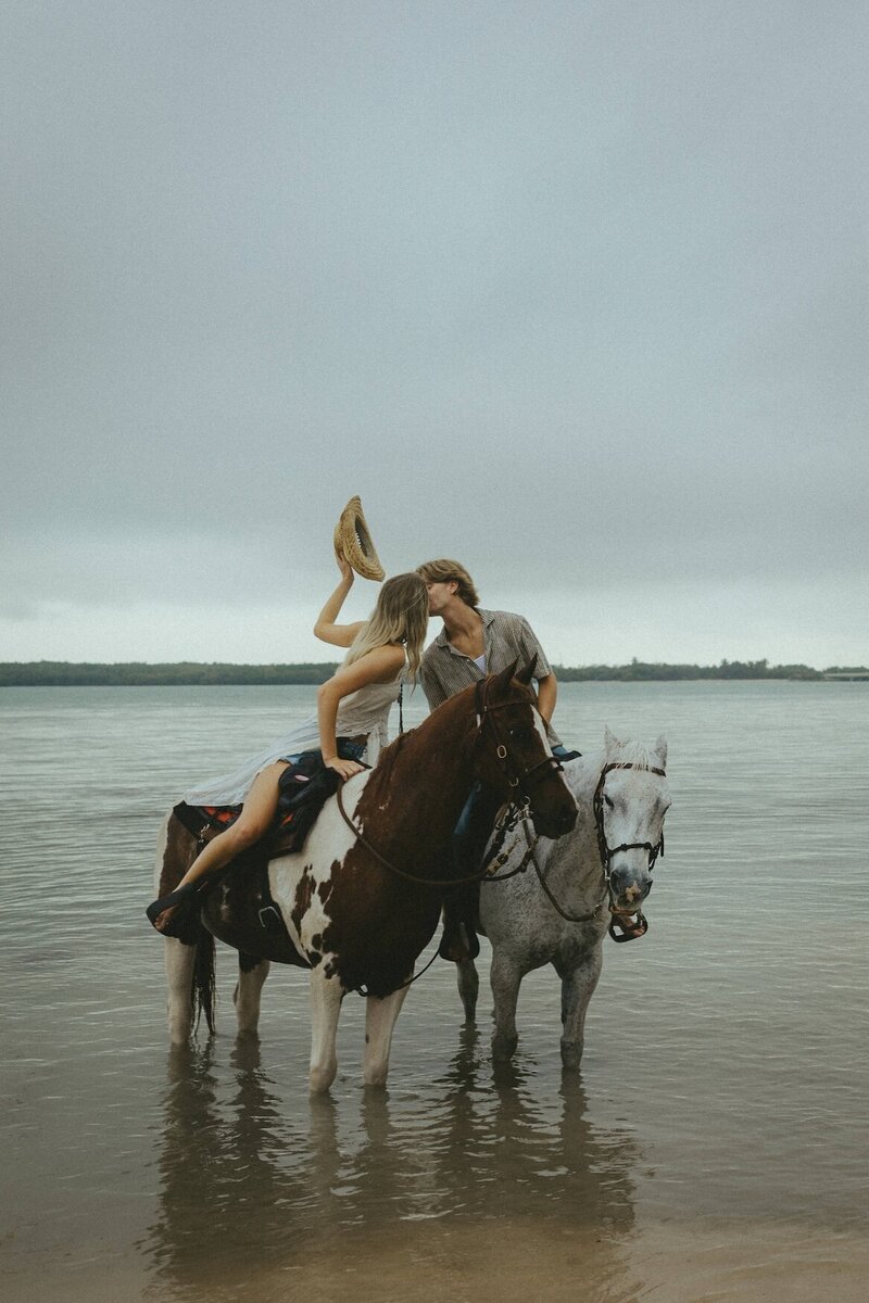 cristina pelino's portfolio image of couple kissing while riding horses on the beach in south florida