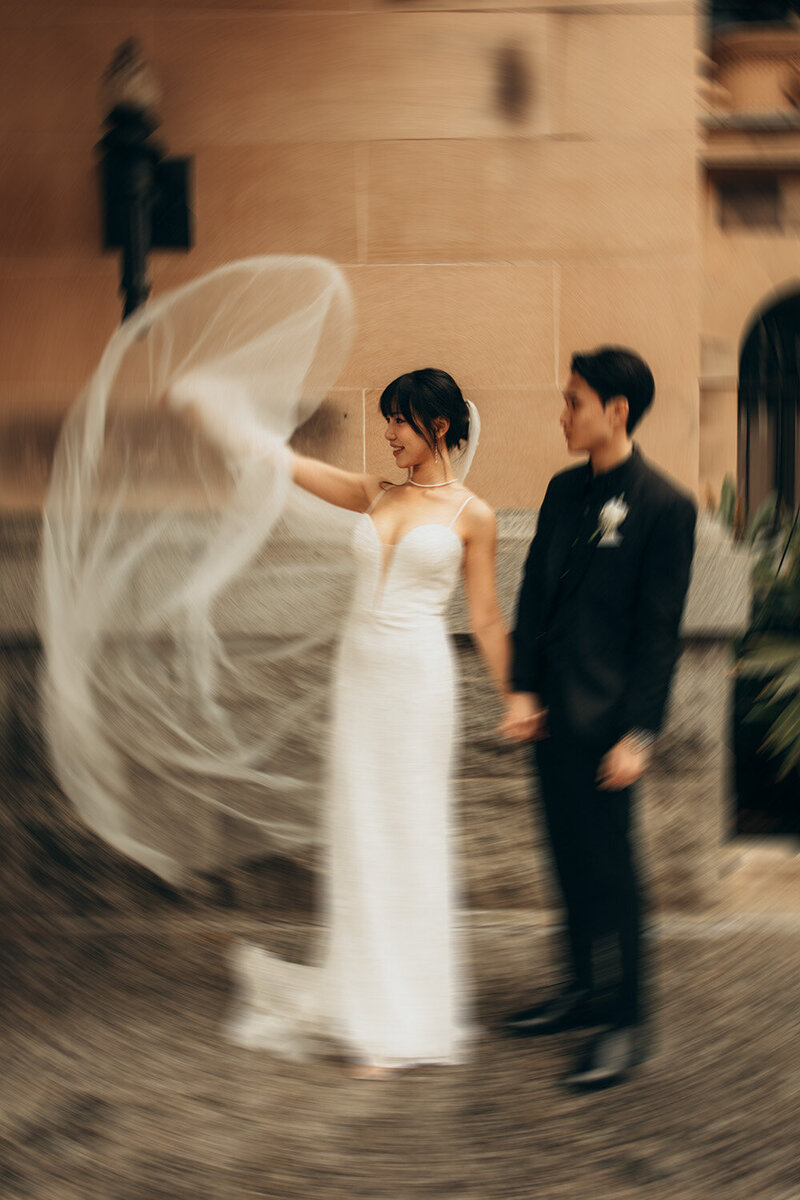 Newly weds holding hands in an urban setting waving her veil 