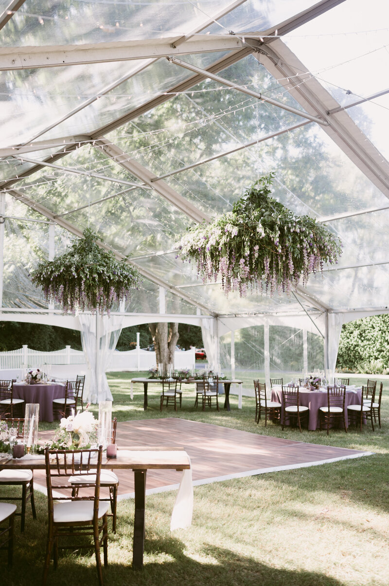 Lush floral chandeliers hanging from clear tent ceiling, lush with romantic violet and cream hanging snap dragons