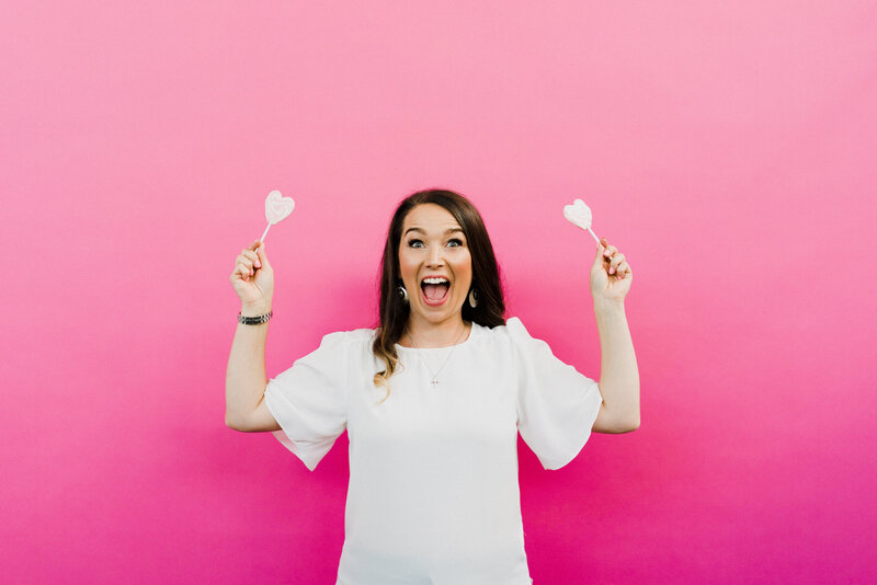Amber Leach of Plymouth Marketing Agency Established By Her holding up heart shaped lollies in front of a pink backdrop