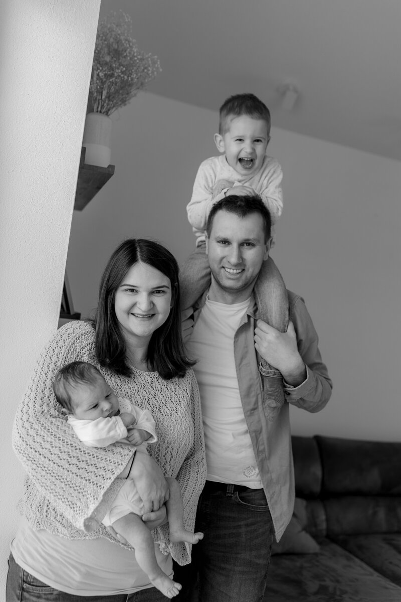 Schwarz weiß Bild von Familie, Mutter hat Baby auf dem Arm und Vater hat Sohn auf den Schultern