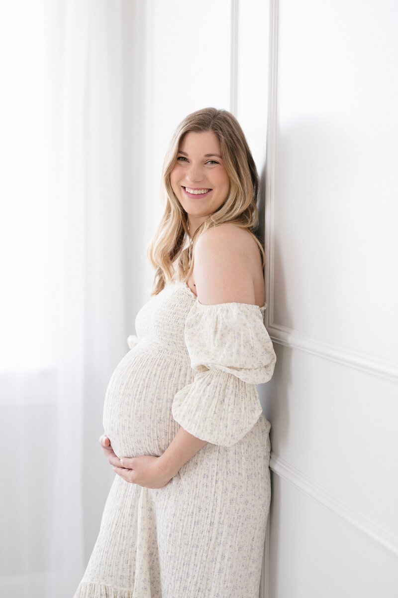 Pregnant mom wearing a Nothing Fits But dress and leaning against a wall in a Louisville maternity studio