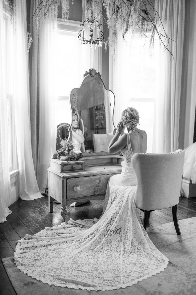 Black and white photo of bride facing away and looking into mirror putting in earrings