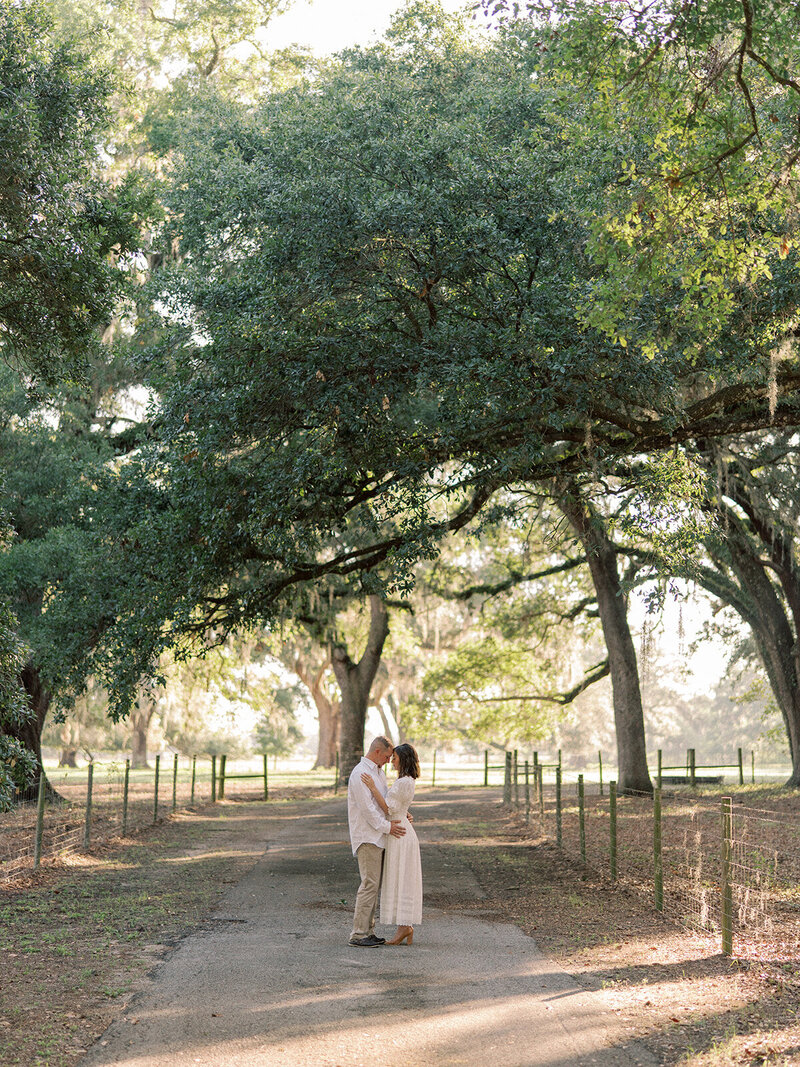 Couple on a road with big oak trees hanging over them.