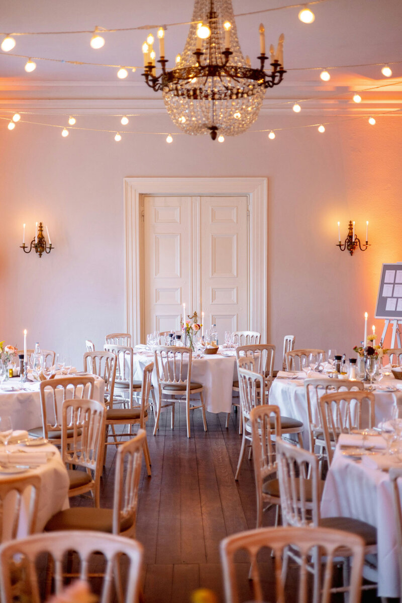 Indoor wedding reception with round tables, candles, and string lights