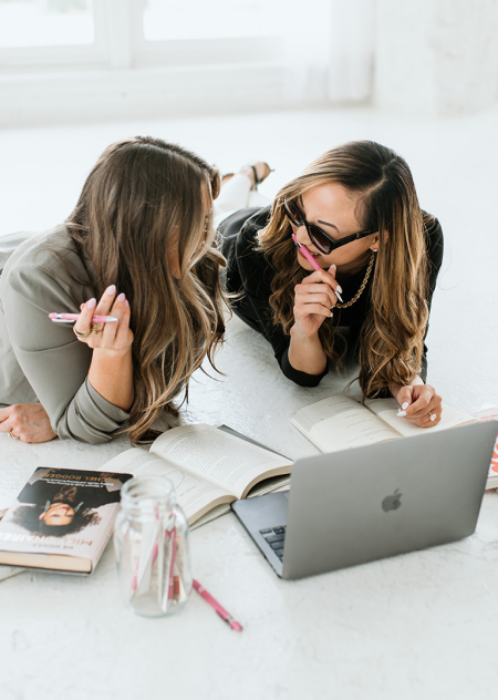 Picture of two women working with a laptop holding pencils