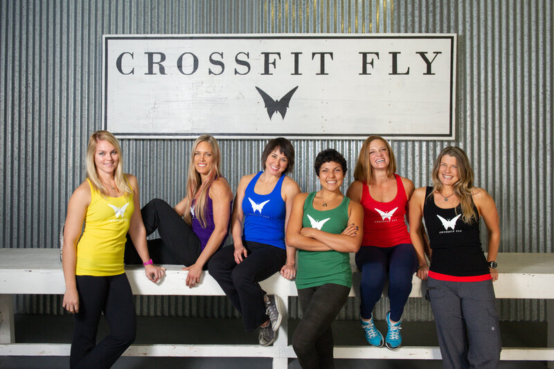 A team photo of the woman owned business Crossfit Fly featuring six female fitness trainers wearing different colored tank tops with a butterfly on front.