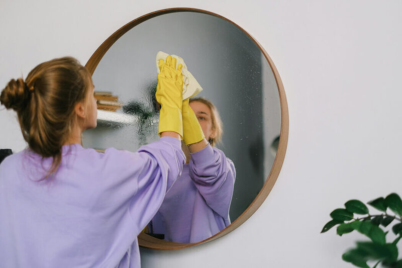 Woman in a purple sweatshirt cleaning a round mirror