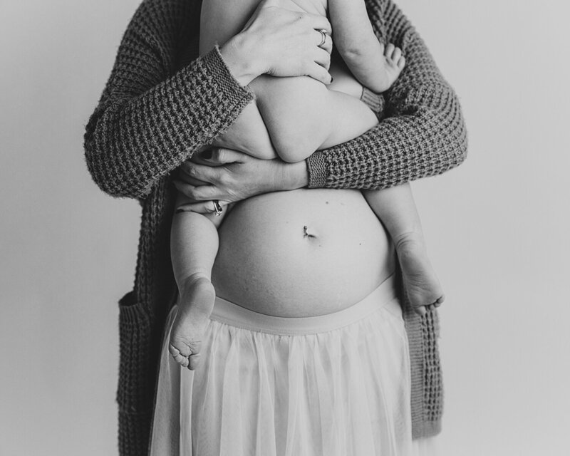 Black and white portrait of a pregnant mother holding her toddler, highlighting her bare baby bump and intimate connection – Fort Collins maternity and motherhood photography