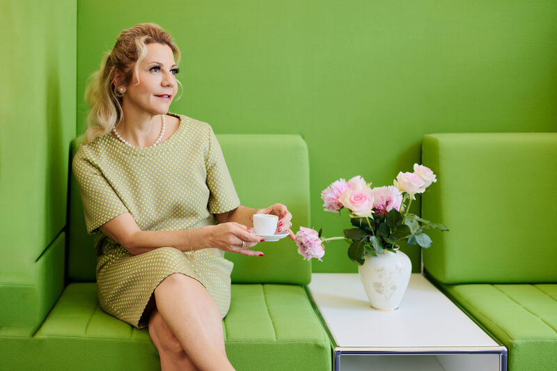 Roxana in a green dress, having a coffee on a green sofa