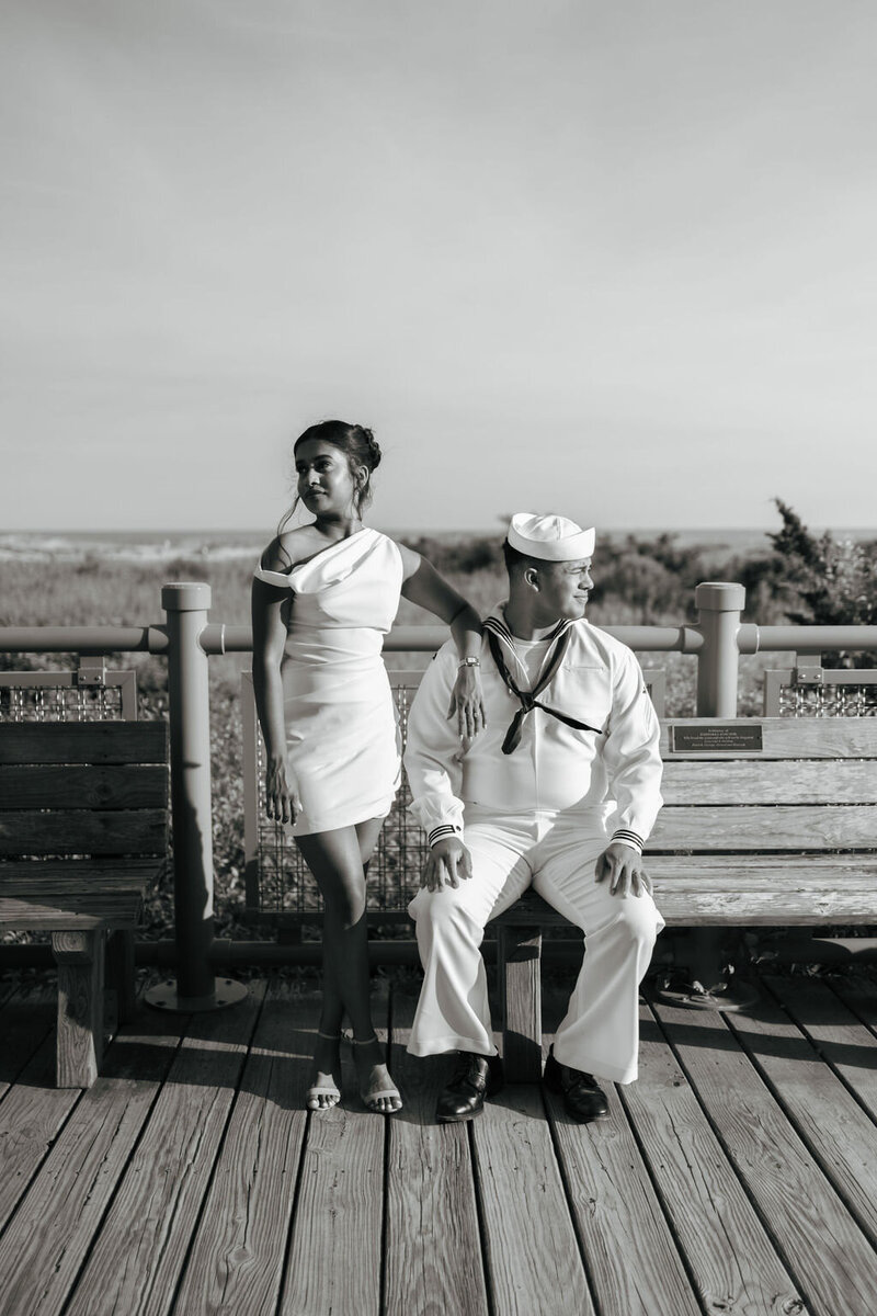 Black and white photo of bride in a short non-traditional wedding dress by her husband in his US Navy sailor uniform at the coast at Robert Moses State Park in Long Island, NY | Emma Leeann Photography