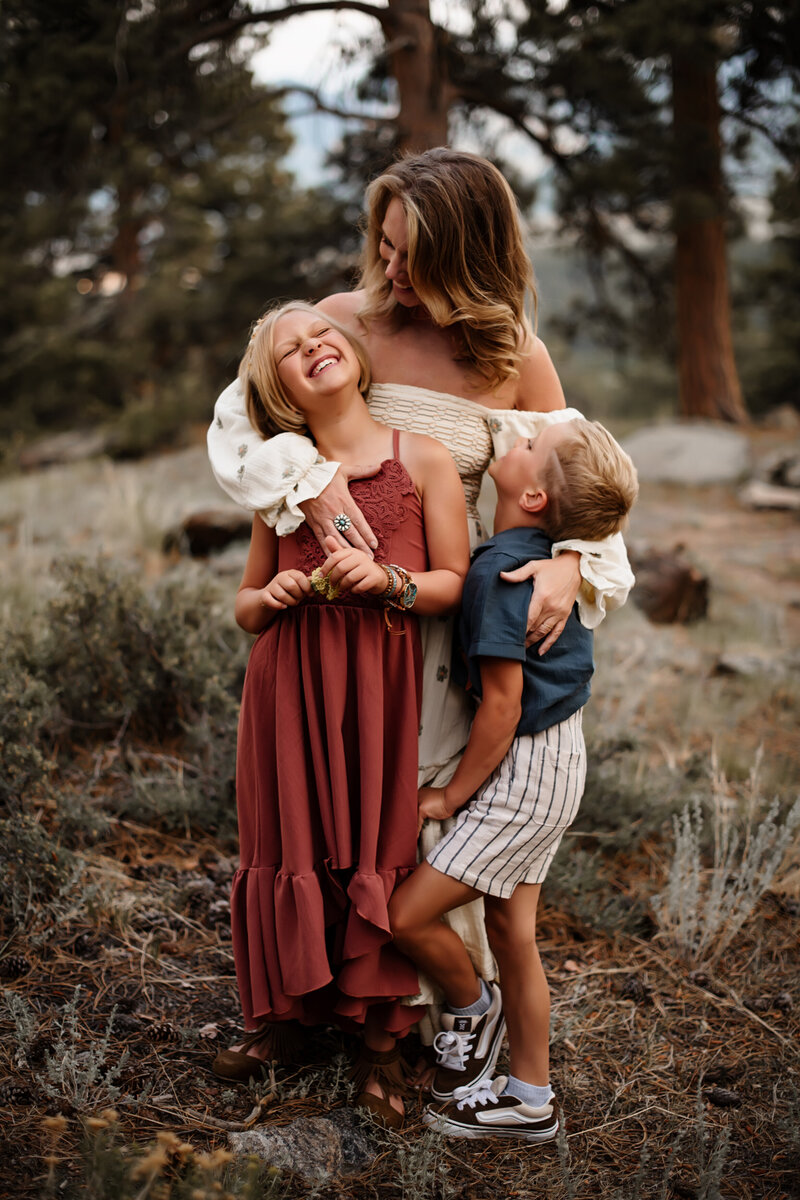 A mother holds her two children while they all laugh together standing in Rock Mountain National Park. 