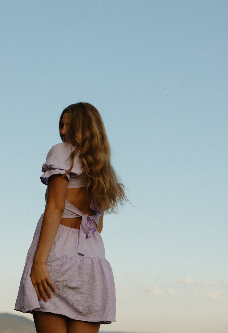 Headshot in an indoor white studio of a woman. She has blond hair, green eyes, and is wearing a matching olive green set.