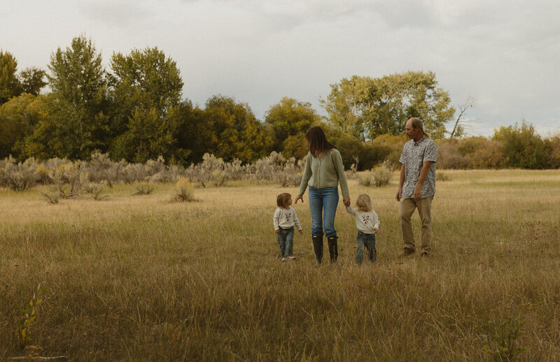 A large family consisting of 10 people and a baby all holding hands, walking towards the camera, and smiling at each other outside.
