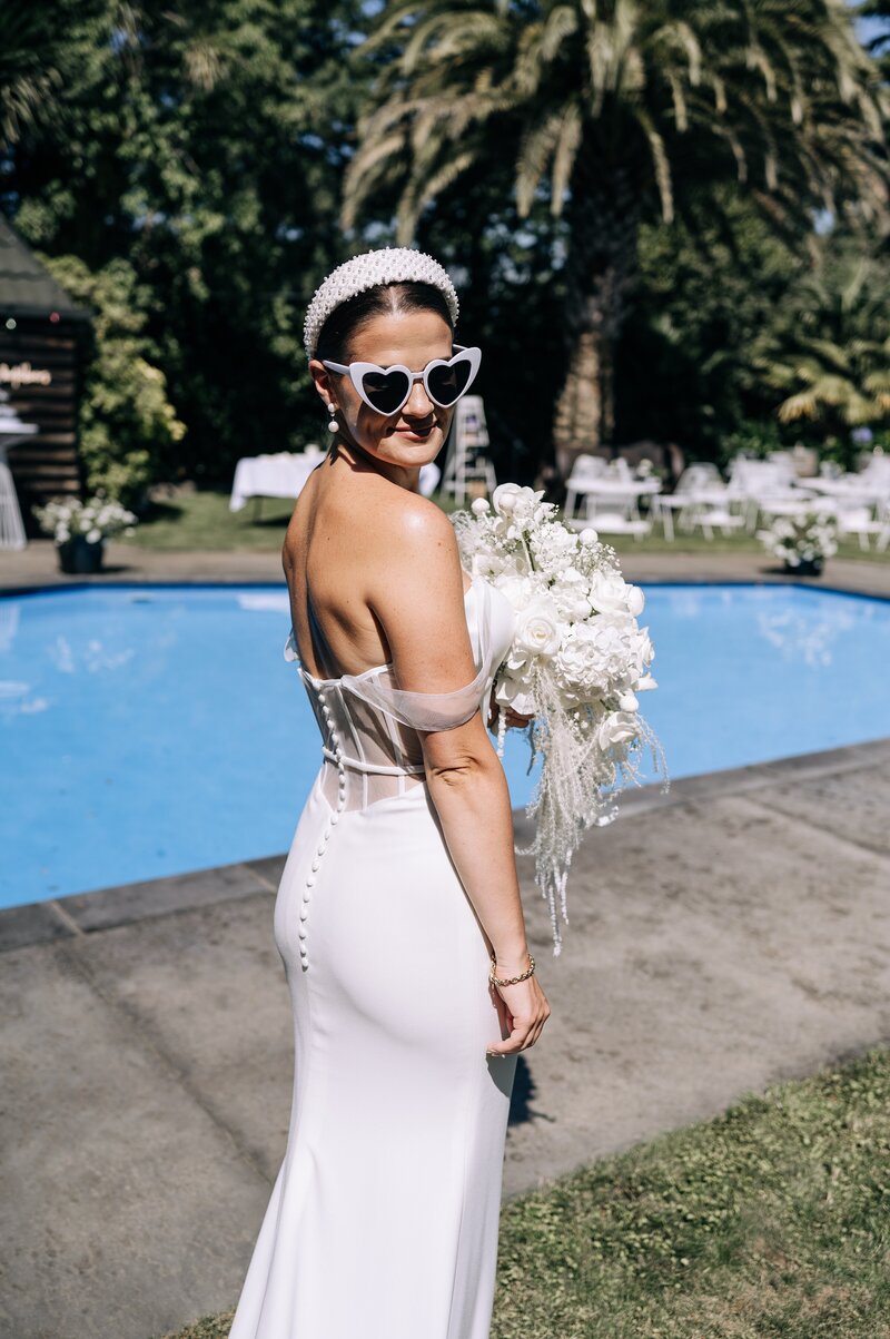 bride in beaded headband and trish peng dress looks over shoulder while holding white cascading bouquet beside her christchurch pool