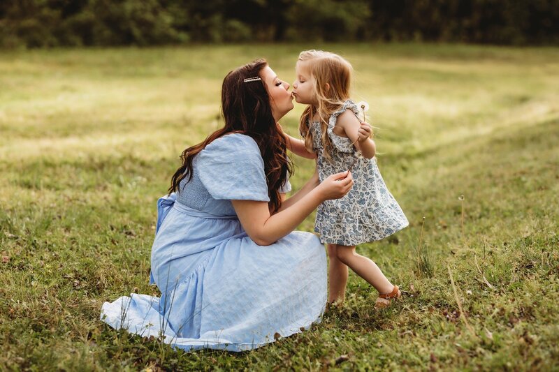 mommy and little girl sharing a kiss in a field