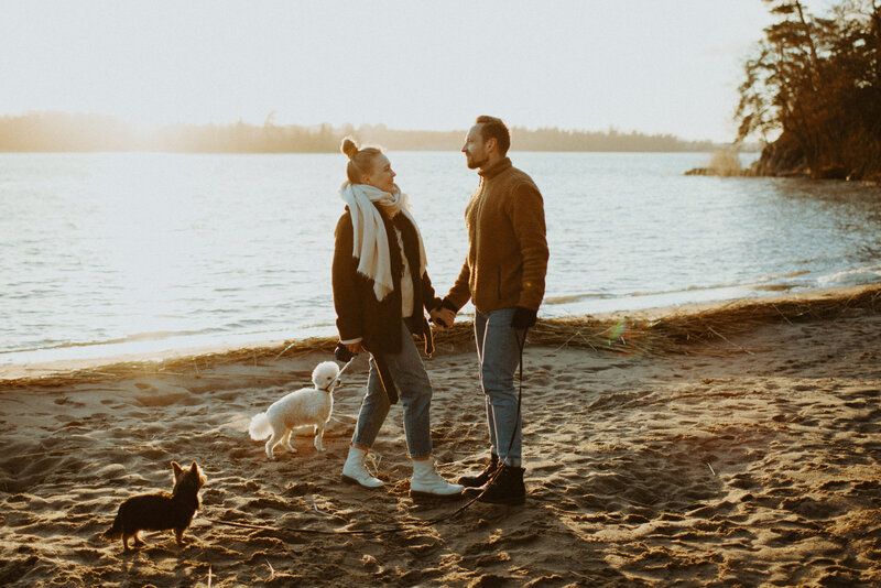 Kihlapari seisoo käsi kädessä kahden koiransa kanssa Kivenlahden uimarannalla Espoossa