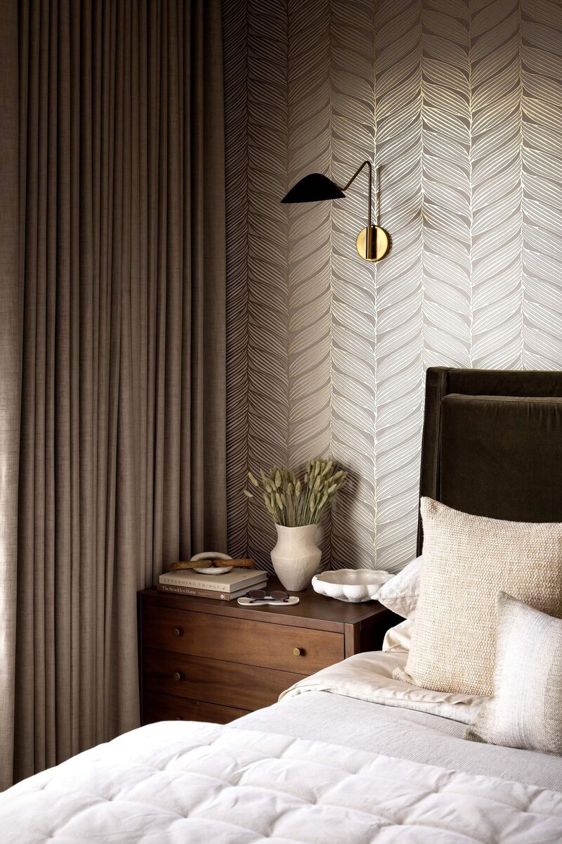 Tranquil bedroom retreat with olive hued upholsterd headboard and metallic leaf design wallpaper.