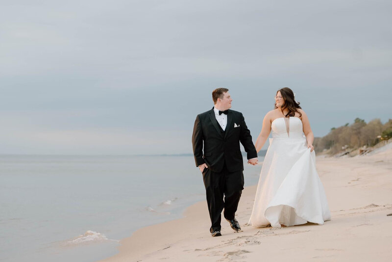 A bride and groom walk on the beach in Grand Haven at sunset