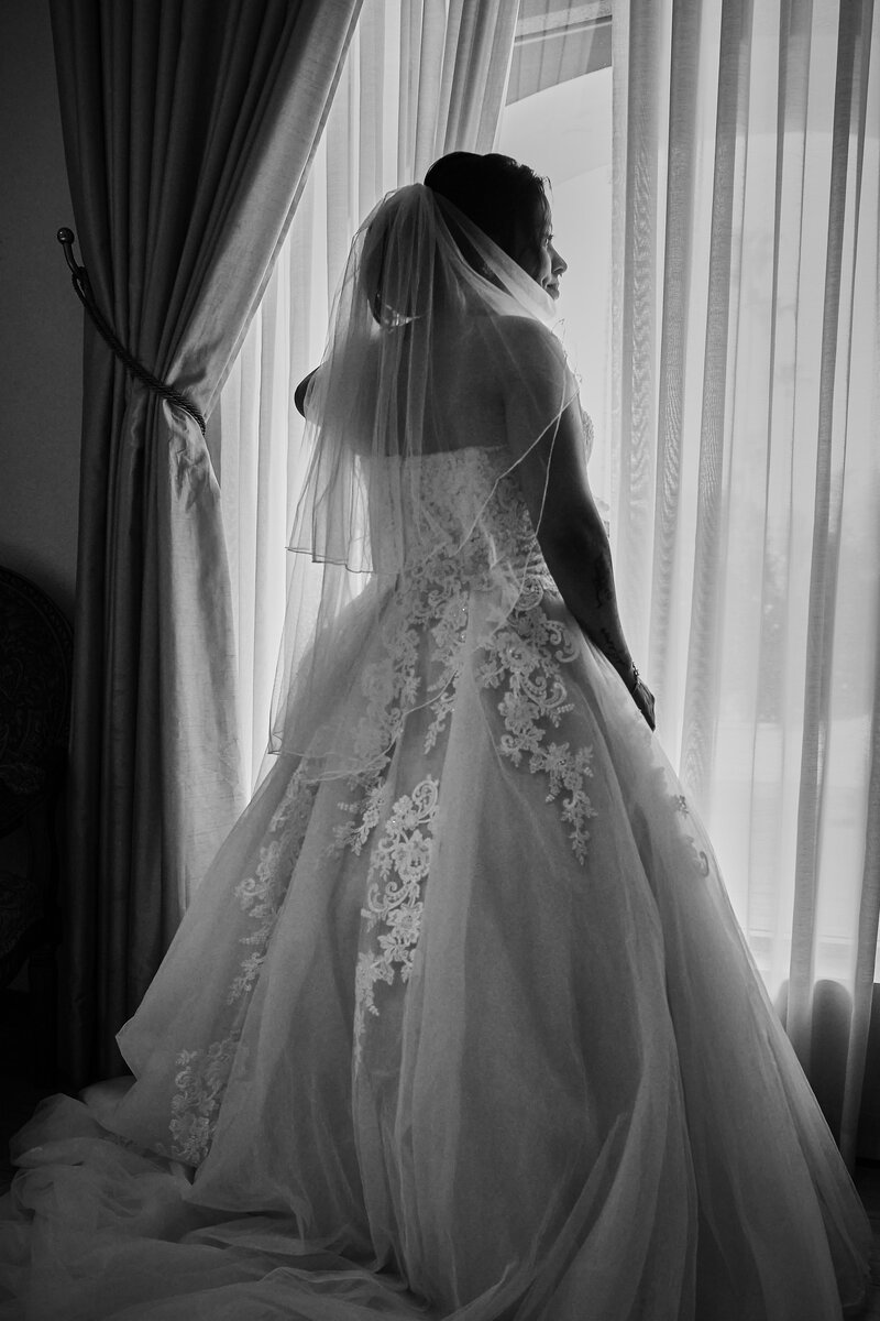 Beautiful bride in her wedding gown looks out the window