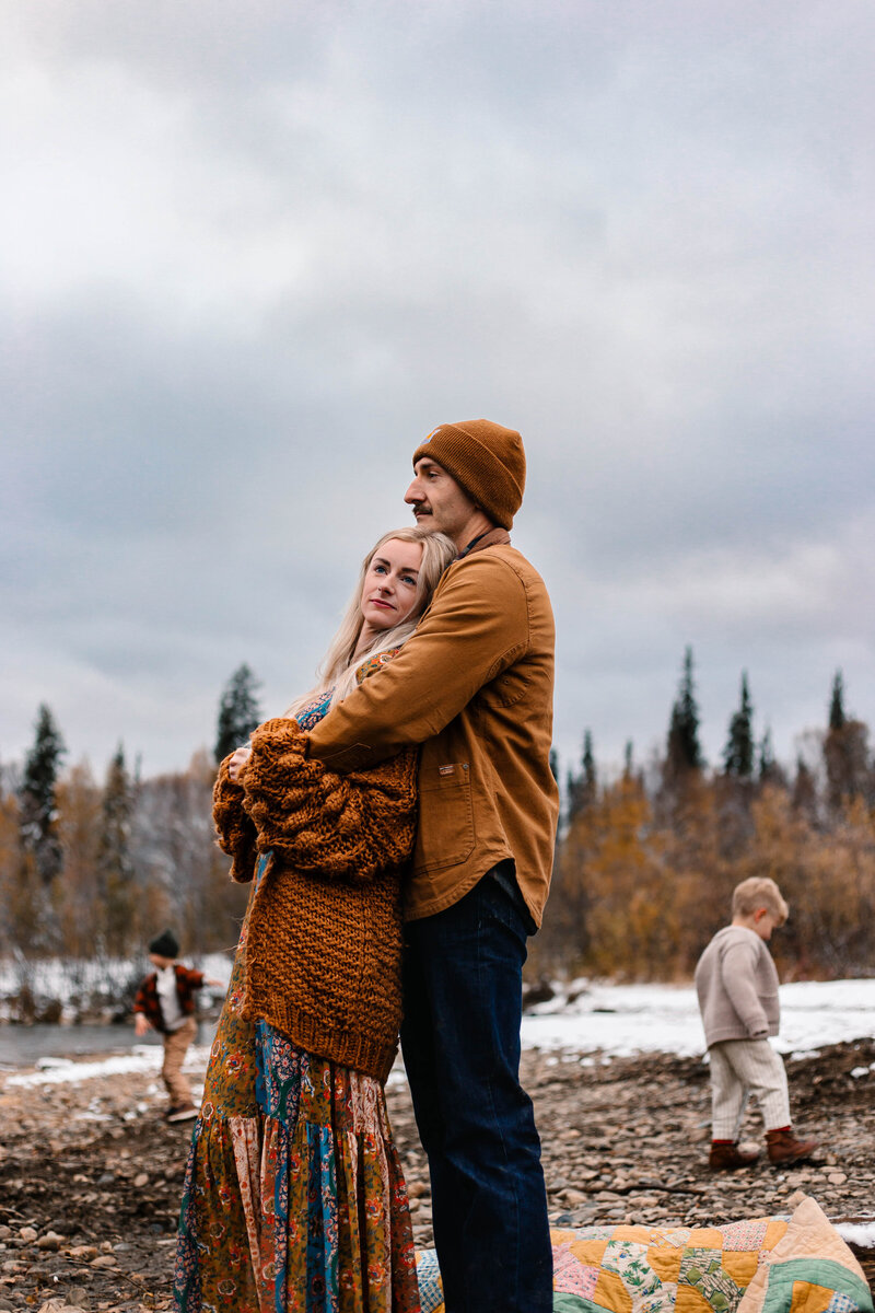 Husband holds his wife while their young children explore Alaskan the nature around them.