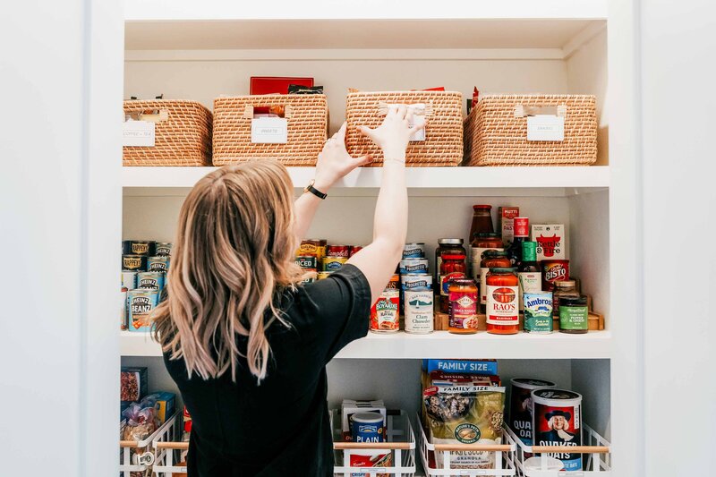 A home organizer placing a basket of food items within a kitchen pantry