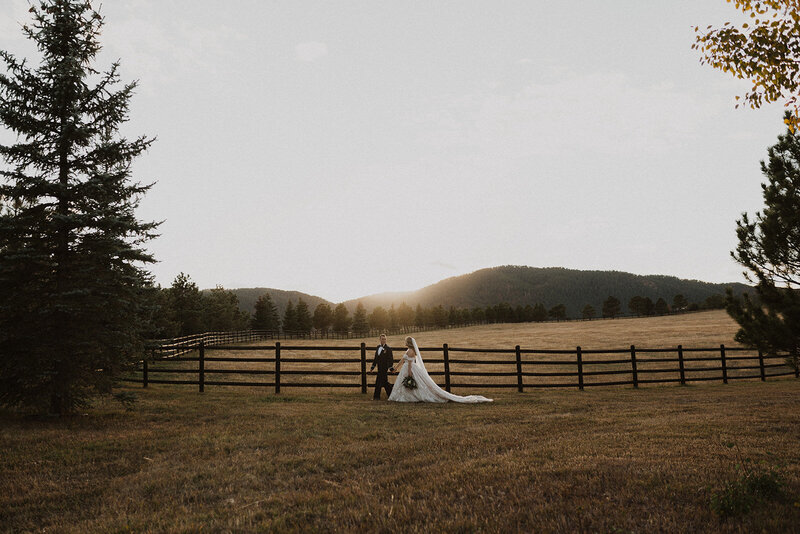Bride and Groom walking through field at Spruce Mountain at sunset.