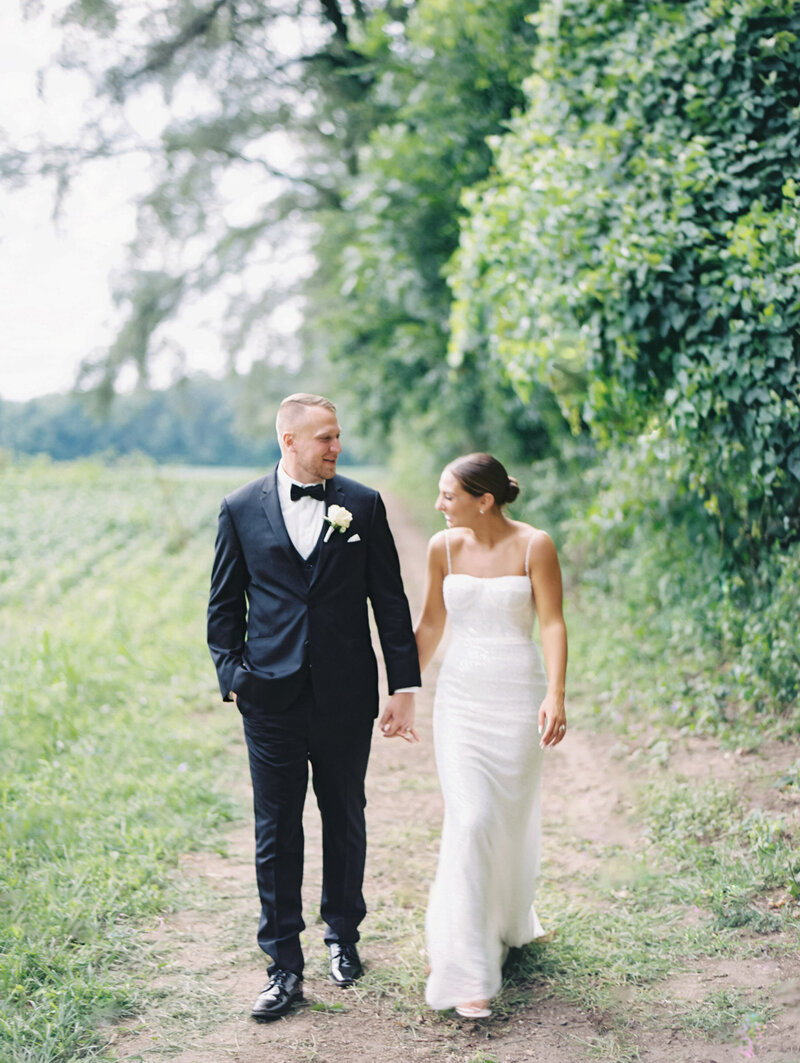 Bride and groom holding hands while walking down dirt path photographed by Chicago and destination editorial wedding photographer Arielle Peters