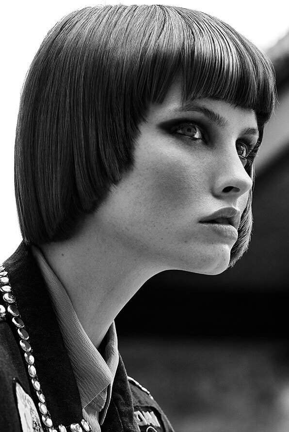 Sleek, geometric bob haircut with sharp lines and a glossy finish, paired with a studded jacket and collared shirt.