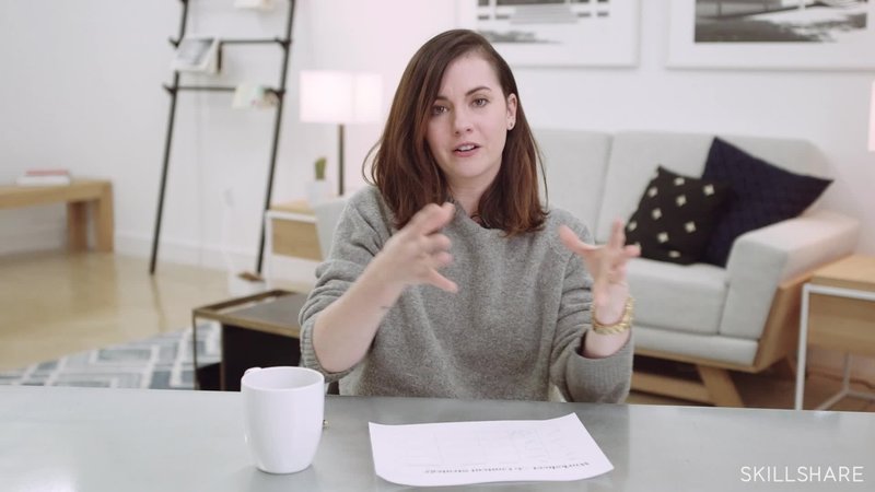 Woman sitting at a table  with a coffee cup and paper looking at the camera