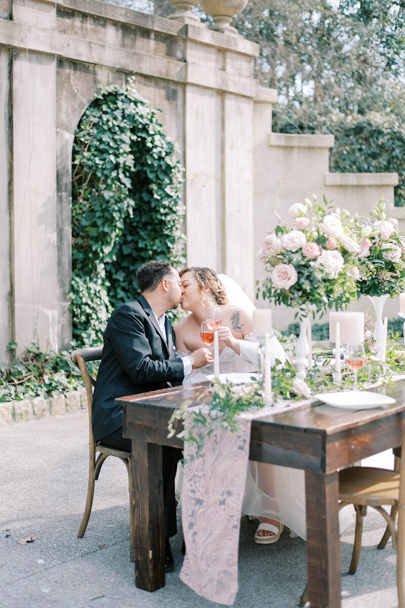 bride and groom sitting together at a sweethearts table at the Swan House in central Florida with the couple leaning into each other and kissing with drinks in their hands