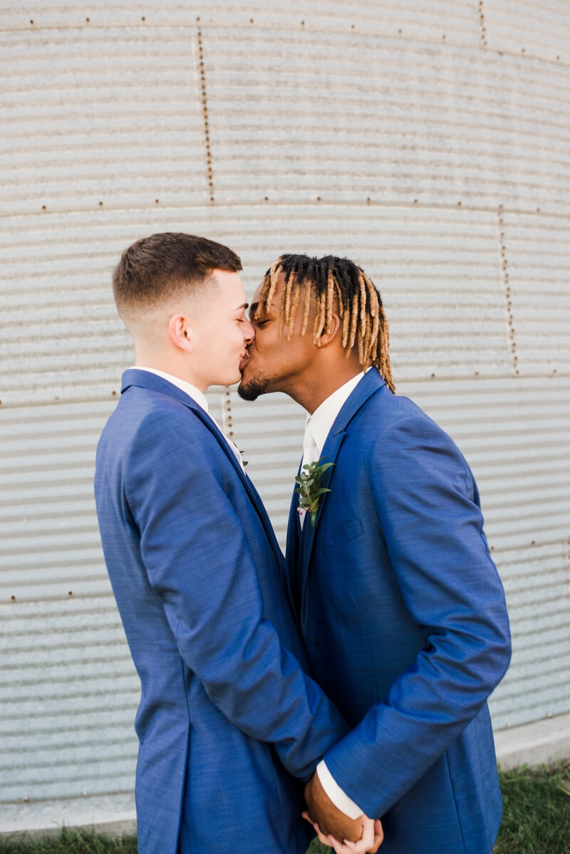 Groom and Groom embrace in a kiss while holding hands