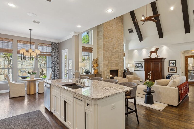 Open-concept kitchen and living room at 1500 Cayman Drive in Allen, Texas, featuring vaulted ceilings, exposed beams, and a stone fireplace.
