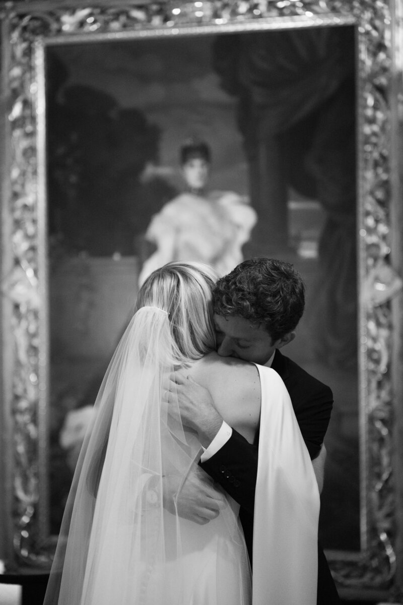 Bride and groom sharing emotional embrace in front of large classical portrait painting