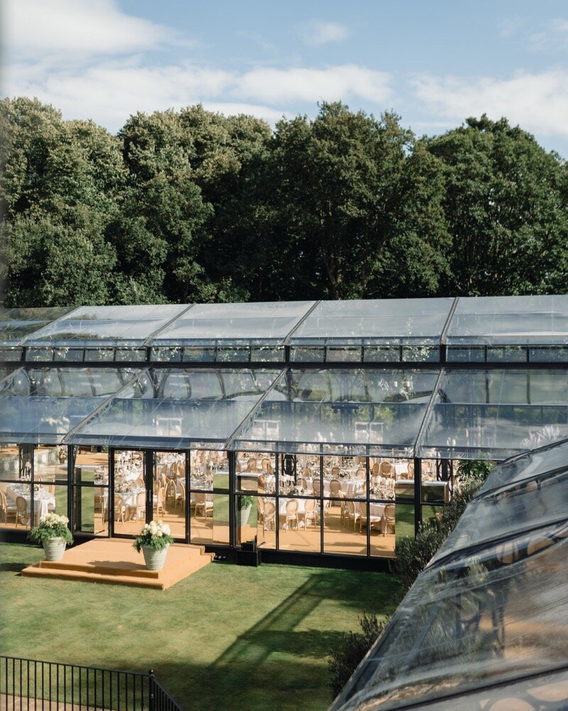 An aerial view of a glass marquee on a lawn with a long walkway and flowers at the entrance for Amelia and Olly Murs