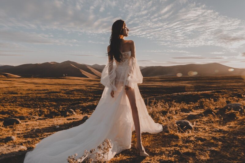 A bride photographed in the golden evening light in a wild field with. mountains in the background.