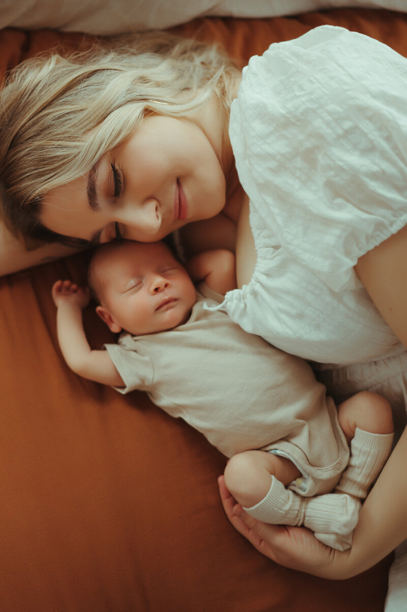 A new mom snuggling her newborn baby boy on their bed.