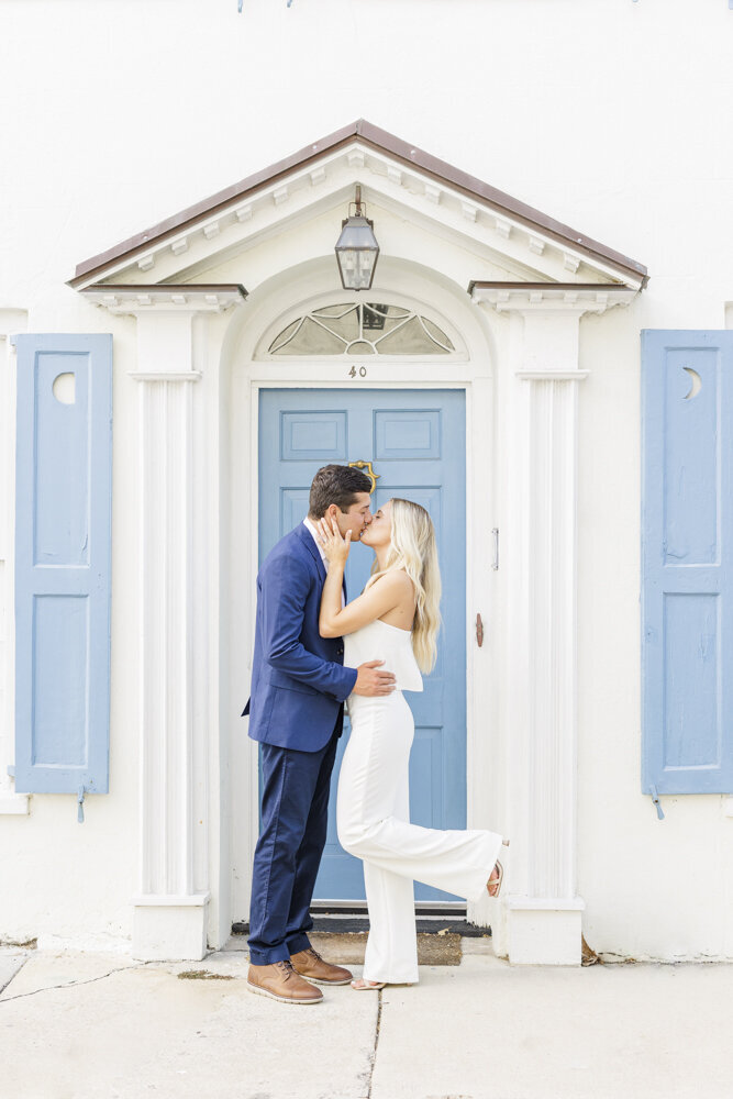 Engaged couple kissing in front of a blue door