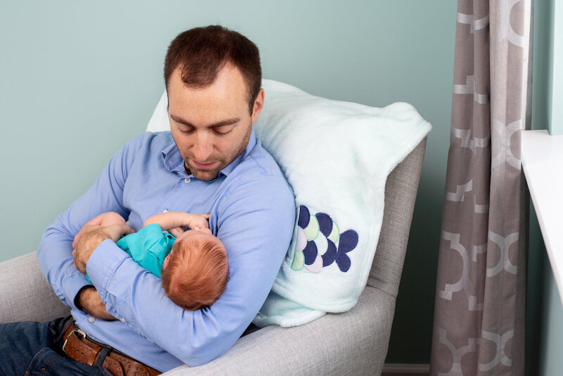 A dad sitting and holding his newborn son.