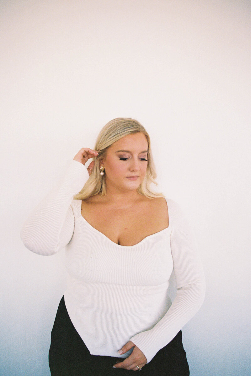 Wilmington Wedding Photographer Leslie DeAnn stands in a white blouse and black pants pulling her blonde hair behind her ear