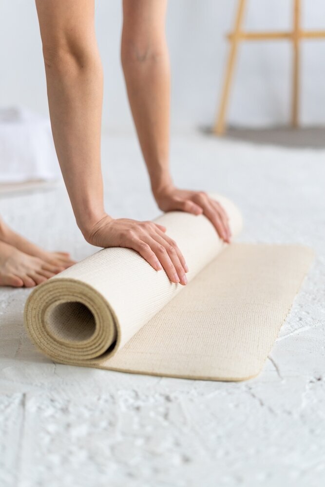 A woman rolls out a white yoga mat for a hypermobility yoga class