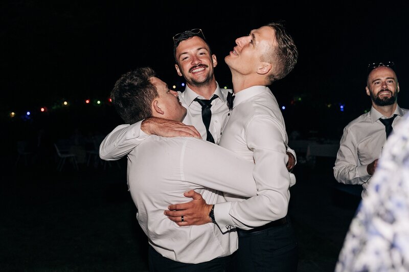 three groomsmen hug and sing together at a christchurch wedding