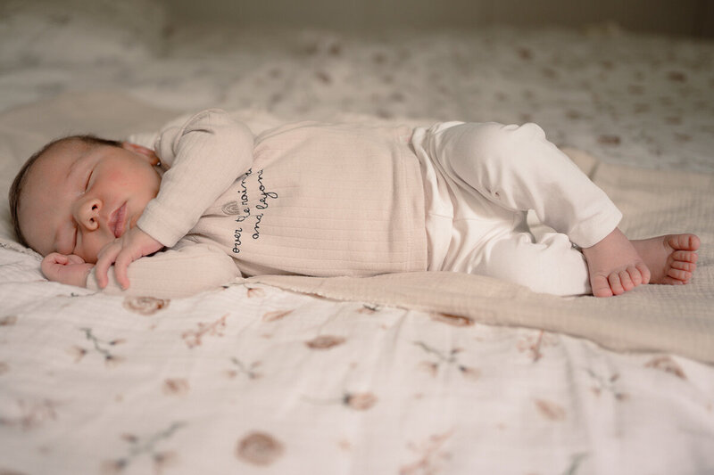 Baby ligt lekker te slapen op bed op zijn zij tijdens een newbornshoot