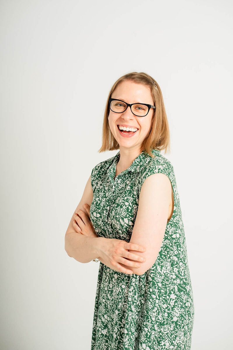 Stephanie laughs while looking towards the camera with her arms crossed.