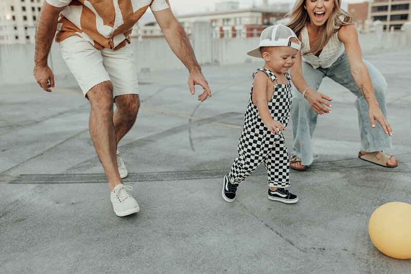 Candid family photo of a mom and dad chasing their young son around on the top of a parking garage