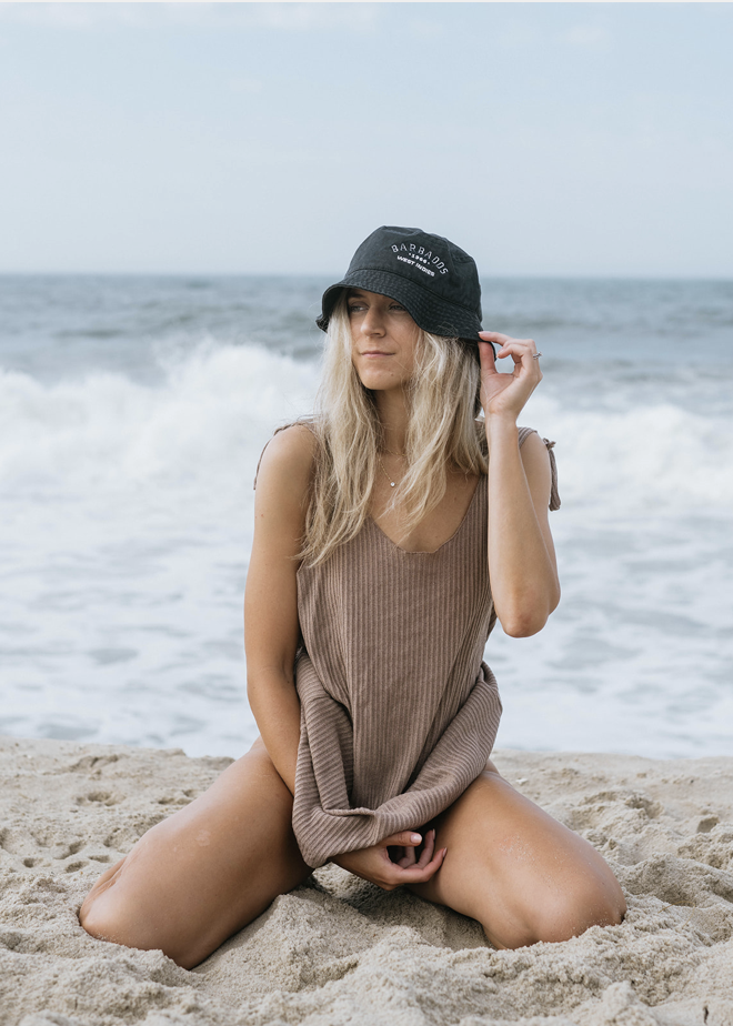A blonde woman on the beach in a tan cover up posing for a brand photography shoot