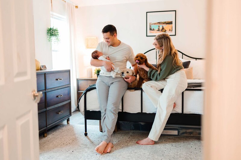 The best family photography in Albuquerque with this tender moment of joy. The image features a dad kissing his partner while they sit on the bed with their newborn baby.
